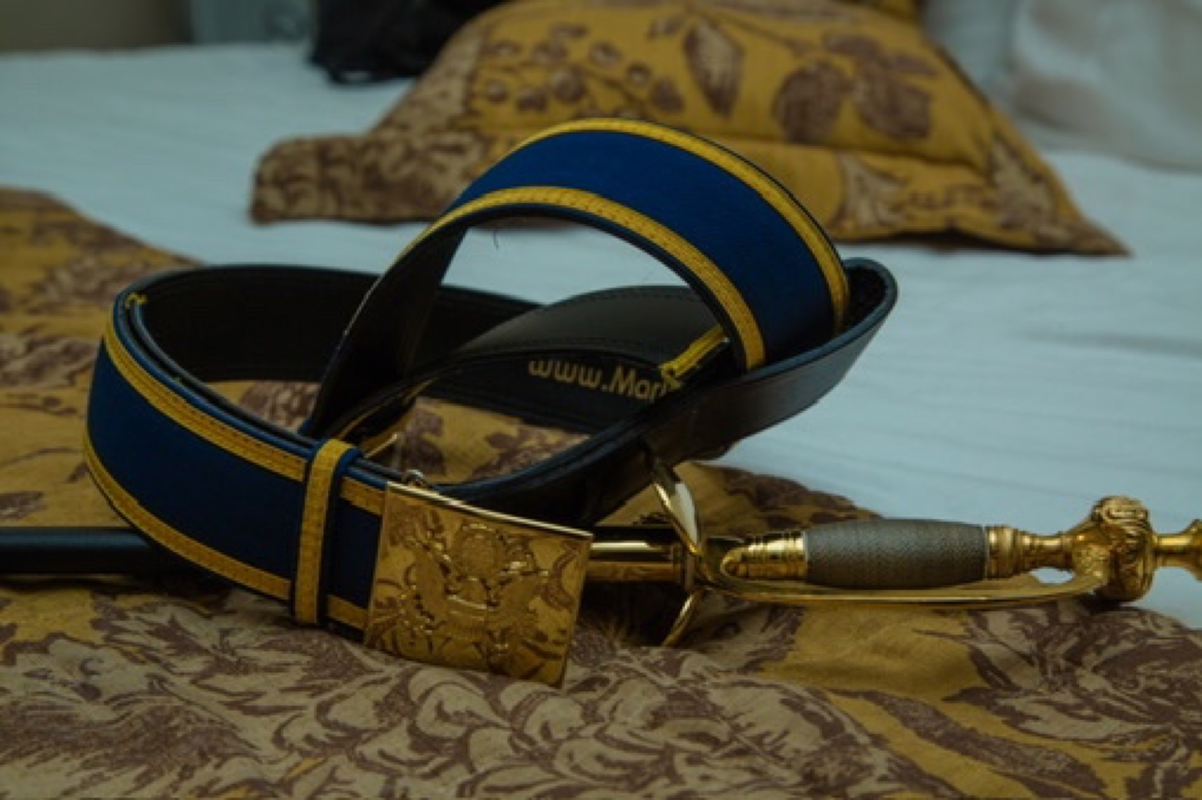 Saber and dress blues belt on the bed.